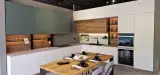 Cucina AR-DUE ad angolo verde salvia e bianco con zona soggiorno, top effetto pietra e tavolo in rovere, vista d'insieme