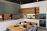 Cucina AR-DUE ad angolo verde salvia e bianco con zona soggiorno, top effetto pietra e tavolo in rovere, vista d'insieme