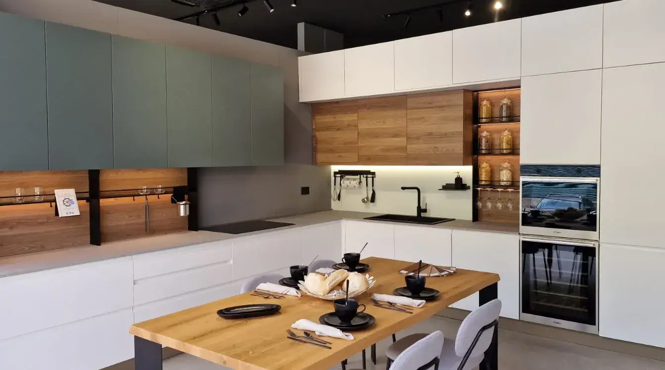 Cucina AR-DUE ad angolo verde salvia e bianco con zona soggiorno, top effetto pietra e tavolo in rovere, vista d'insieme