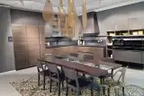 Cucina AR-TRE Up Design ad angolo in olmo scuro con top Fenix nero, cappa a piramide, parete forni e tavolo in legno massello, vista d'insieme della composizione
