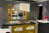 Cucina moderna grigia con isola centrale, piano in quarzo bianco e dettagli gialli a giorno