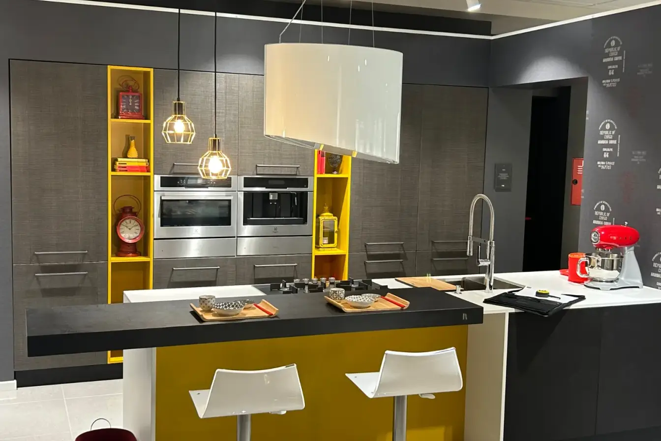 Cucina moderna grigia con isola centrale, piano in quarzo bianco e dettagli gialli a giorno