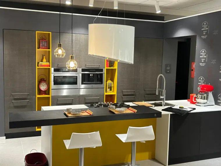 Cucina moderna grigia con isola centrale, piano in quarzo bianco e dettagli gialli a giorno