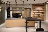 Isola della cucina Prima Gola Linear con top in gres nero dorato, piano cottura a induzione e lavello nero, con penisola snack in Fenix nero e due sgabelli