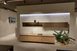 Zona soggiorno coordinata alla cucina Prima Gola Linear con madia sospesa in laccato pesca opaco, pensile in gessato noce e mensola a giorno illuminata