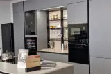 Parete di colonne della cucina Stosa Metropolis in PET Grigio con vano a giorno illuminato, forno e microonde da incasso e isola Aliant in primo piano
