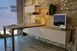 Zona soggiorno coordinata alla cucina Stosa Young: madia sospesa da 270 cm, pensile con vano a giorno illuminato e tavolo alto snack in esposizione