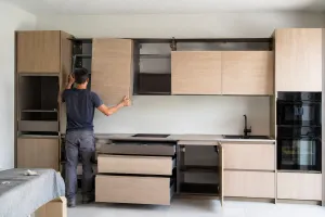 Montaggio di una cucina in legno chiaro con basi, colonne e pensili durante l'installazione dei moduli