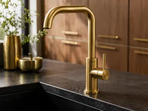 Rubinetto cucina in ottone spazzolato su lavello nero e piano scuro, coordinato con maniglie in ottone su mobili in legno